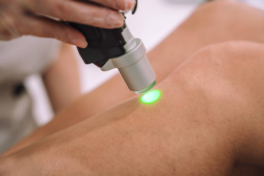 Feche a foto da mão enluvada com a peça de mão da máquina de depilação a laser nas perna da mulher.