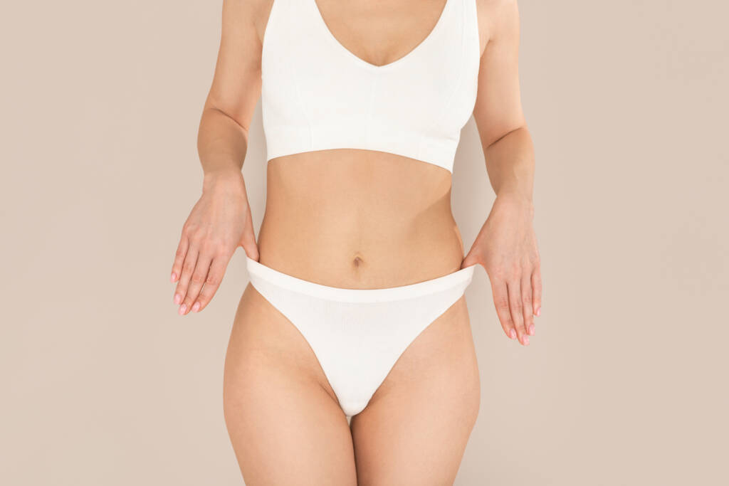 Jovem irreconhecível e bem ajustada posando de roupa íntima branca, mostrando um corpo sexy e liso, sem pelos na região intima
